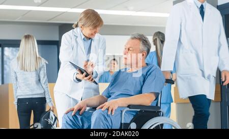 Im Krankenhaus zeigt eine Ärztin einem älteren Patienten einen Tablet-Computer und erklärt seinen Zustand. Modernes Krankenhaus mit bester Betreuung. Stockfoto