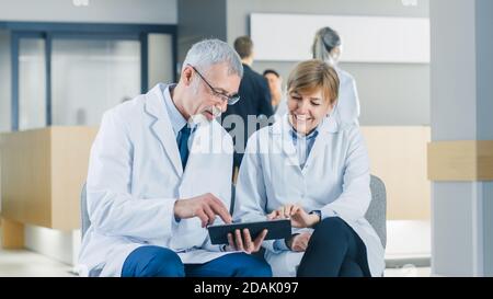 In der des Krankenhauses zwei professionelle Arzt haben Diskussion, mit Tablet-Computer, während Sie in der Lobby sitzen. Sie Verwenden Tablet-Computer. Sauber Stockfoto