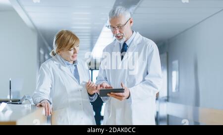 Im Krankenhaus stehen zwei Ärzte an der Rezeption, sprechen und teilen Informationen über Tablet-Computer. Moderne Krankenhaus mit Patienten und Stockfoto