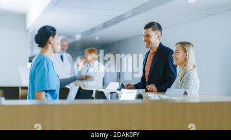 Im Krankenhaus an der Rezeption Krankenschwester auf Dienst Antworten junge Paar Patienten und zeigt ihnen einen Weg. Stockfoto