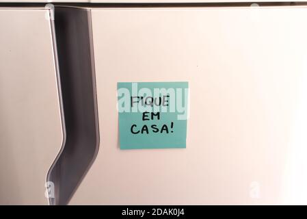 Haftnotiz auf dem Kühlschrank mit dem Hinweis zu Hause bleiben! In portugiesischer Sprache (Fique em Casa!) Stockfoto