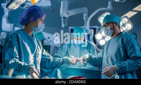Vielfältiges Team von professionellen Chirurgen, die invasive Chirurgie an einem Patienten im Operationssaal des Krankenhauses durchführen. Krankenschwester gibt dem Chirurgen Instrumente aus Stockfoto