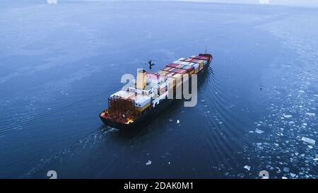 Luftaufnahme des Frachtschiffes, das durch das Meer bewegt. Im Hintergrund Winterlandschaft. Stockfoto