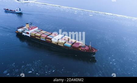 Luftaufnahme des Frachtschiffes, das durch das Meer bewegt. Im Hintergrund Winterlandschaft. Stockfoto