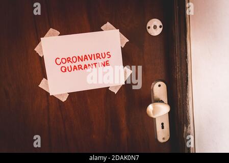 Blatt Papier mit Coronavirus Quarantine Text Hand geschrieben in Rote Buchstaben auf Holztür neben dem Griff getaped Und Schlüsselloch Stockfoto