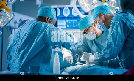 Vielfältiges Team von professionellen Chirurgen, die invasive Chirurgie an einem Patienten im Operationssaal des Krankenhauses durchführen. Chirurgen Verwenden Instrumente. Stockfoto