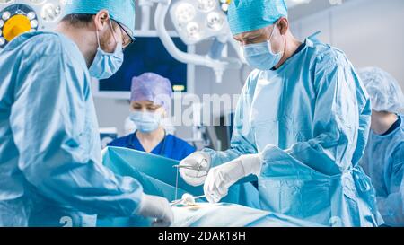 Vielfältiges Team von professionellen Chirurgen, Assistenten und Krankenschwestern, die invasive Chirurgie an einem Patienten im Operationssaal des Krankenhauses durchführen. Chirurgen sprechen und Stockfoto