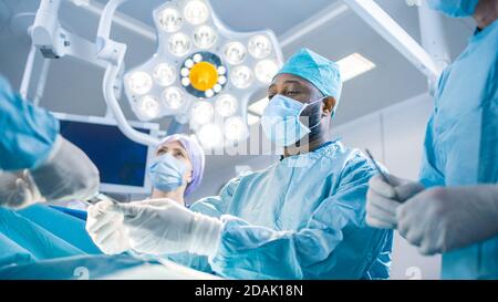 Vielfältiges Team von professionellen Chirurgen, Assistenten und Krankenschwestern, die invasive Chirurgie an einem Patienten im Operationssaal des Krankenhauses durchführen. Chirurgen sprechen und Stockfoto