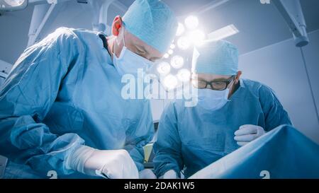 Low Angle Shot im Operationssaal von zwei Chirurgen während des chirurgischen Eingriffs Biegen über den Patienten mit Instrumenten. Professionelle Ärzte in modernen Stockfoto