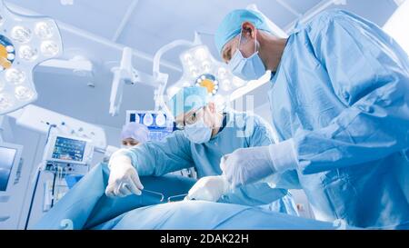 Low-Angle-Aufnahme eines Teams von professionellen Chirurgen, die invasive Chirurgie an einem Patienten im Operationssaal des Krankenhauses durchführen. Chirurgen Verwenden Stockfoto