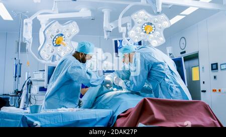 Vielfältiges Team von professionellen Chirurgen, die invasive Chirurgie an einem Patienten im Operationssaal des Krankenhauses durchführen. Chirurgen Verwenden Instrumente. Stockfoto