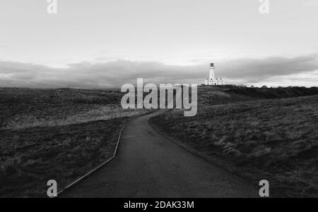 Leuchtturm unter bewölktem Himmel mit Gräsern und Wanderweg, der in der Mitte im Vordergrund bei Sonnenaufgang im Herbst in Flamborough, Yorkshire, Großbritannien, verläuft. Stockfoto