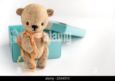 Ein handgefertigter Vintage Teddybär steht neben einer Geschenkbox auf weißem Hintergrund. Geschenk für einen wichtigen Feiertag. Selektiver Fokus. Nahaufnahme. Speicherplatz kopieren. Stockfoto