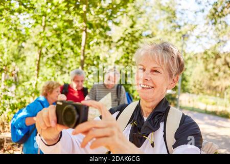 Glückliche ältere Frau mit Kamera vor einer Wanderung Gruppe in der Natur im Sommer Stockfoto