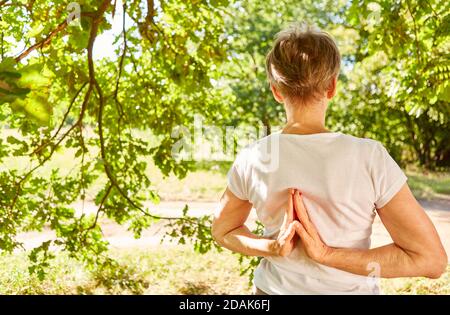 Ältere Frau macht eine Yoga-Meditation mit Händen in der Gebetshaltung hinter ihrem Rücken Stockfoto