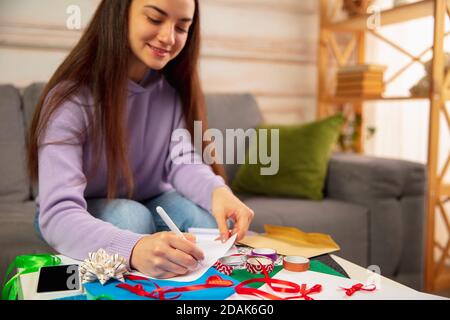 Komfortabel. Frau Schreiben Brief, Grußkarte für Neujahr und Weihnachten 2021 für Freunde oder Familie sitzen zu Hause mit Laptop. Feiertage, Feier. Sieht fröhlich, glücklich, vorsichtig aus. Stockfoto