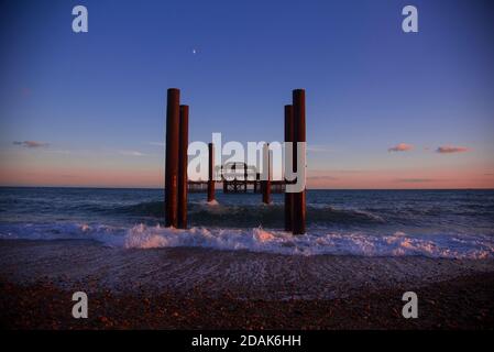 Blick direkt auf die Überreste des Brighton West Pier an der East Sussex Coast. Goldener Himmel und der Mond ist nur über dem Pier sichtbar. Brighton, Großbritannien. Stockfoto