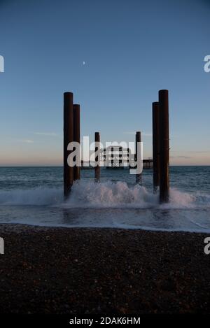 Blick direkt auf die Überreste des Brighton West Pier bei Sonnenuntergang mit einem goldenen Himmel, aufgenommen im Sommer. Wellen krachen gegen die Überreste. Brighton Großbritannien. Stockfoto