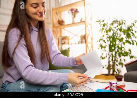 Komfortabel. Frau Schreiben Brief, Grußkarte für Neujahr und Weihnachten 2021 für Freunde oder Familie sitzen zu Hause mit Laptop. Feiertage, Feier. Sieht fröhlich, glücklich, vorsichtig aus. Stockfoto