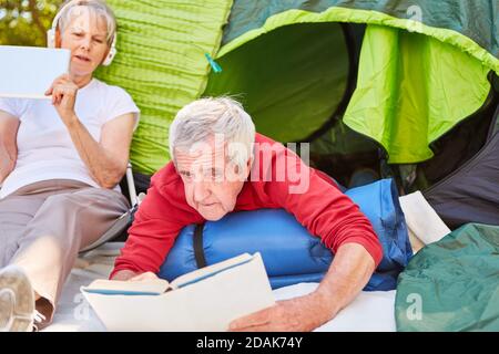 Paar als Rentner auf Outdoor-Camping-Urlaub entspannen mit Lesen Und Musik hören Stockfoto