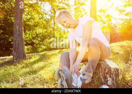 Ältere Frau, die im Park Rollschuhe aufsetzt Sommer Stockfoto