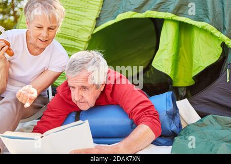 Rentnerpaar entspannen beim Lesen vor dem Zelt Im Urlaub im Freien Stockfoto