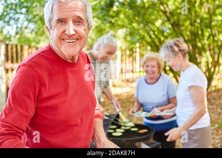 Lächelnde Rentner mit Freunden, die zusammen grillen Der Garten Stockfoto