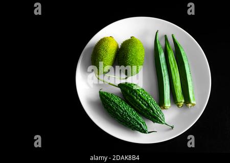 Grünes Gemüse in weißem Teller auf schwarzem Hintergrund. Stockfoto