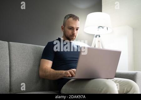 Mann Sitzt Im Sofa Zu Hause Und Mit Laptop Stockfoto