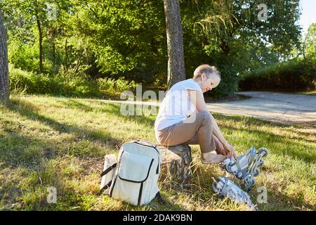 Ältere Frau im Sommer in der Natur auf Rolle setzen Schlittschuhe vor dem Inlineskaten Stockfoto