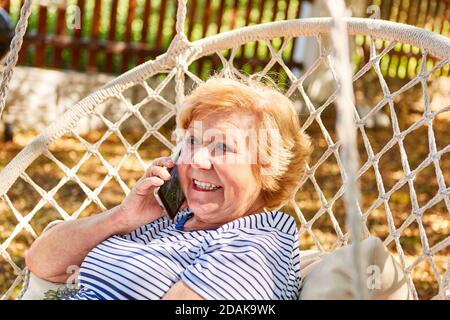 Glückliche ältere Frau im Gespräch am Telefon mit Smartphone in Der Garten im Sommer als Rentner Stockfoto