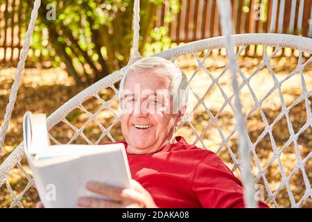 Rentner glücklicher älterer Mann, der im Sommer im Garten ein Buch liest Stockfoto