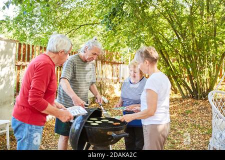 Gruppe von Senioren als Freunde mit einem Grill zusammen in Der Garten im Sommer Stockfoto