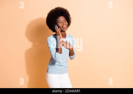 Foto-Porträt von schönen lockigen dunkelhäutigen Mädchen sprechen Auf Handy lachen mit geschlossenen Augen isoliert auf beige Farbiger Hintergrund Stockfoto