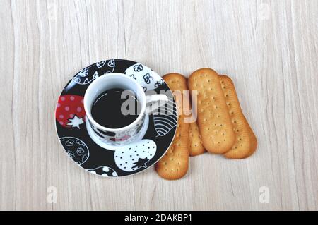 Tasse Kaffee, Kaffee mit Keksen in farbiger Tasse und schwarzer Untertasse mit handgezeichneten Zeichnungen, Butterkekse auf Holzhintergrund mit Kopierfläche Stockfoto