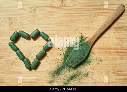 Chlorella oder Spirulina Tabletten und Pulver in einem Holzlöffel auf einem hellen Holzhintergrund. Nahrungsergänzungsmittel, Detox Superfood. Draufsicht. Stockfoto
