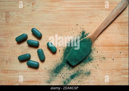 Chlorella oder Spirulina Tabletten und Pulver in einem Holzlöffel auf einem hellen Holzhintergrund. Nahrungsergänzungsmittel, Detox Superfood. Draufsicht. Stockfoto