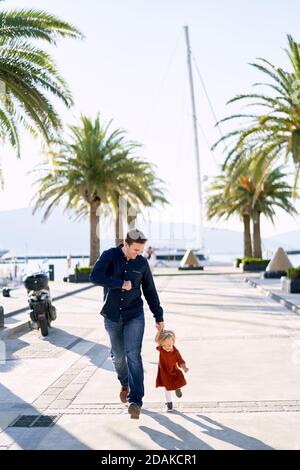 Vater und Tochter laufen Hand in Hand daneben Palmen am Meer Stockfoto