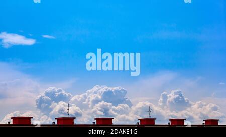 Massive Wolken in der Ferne am blauen Himmel. Das Foto wird vom Dach des Hauses mit den Aufzugsmaschinenräumen umrahmt.(6 kleine Häuser am Stockfoto