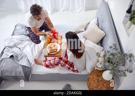 Draufsicht auf junge kaukasische Paar mit Frühstück im Bett. Weiblich überrascht von eingewickelten Geschenk von einem Mann Stockfoto