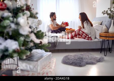 Junge kaukasischen bärtigen Kerl überraschend seine Freundin mit Weihnachtsgeschenk Beim gemeinsamen Frühstück im Bett Stockfoto