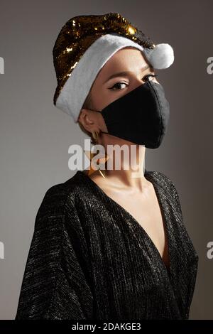 Frau mit goldenem weihnachtshut, schwarze medizinische Maske. Mode-Stil mit glänzenden Kleidung und Accessoires für Weihnachten Zeit. Schützen Sie sich vor Coronavirus C Stockfoto