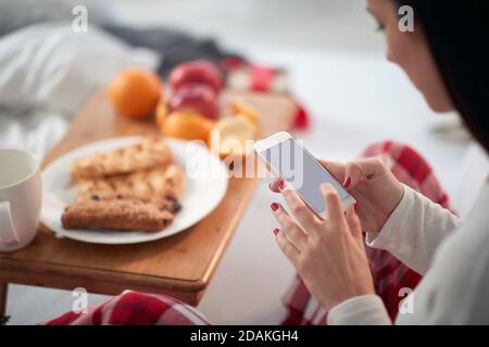 Detail schöne kaukasische Brünette mit Frühstück im Bett in Pyjamas zu Weihnachten, SMS auf Handy. Copy space Stockfoto