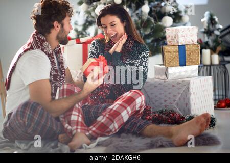 Liebevolles Paar teilt Geschenke an Weihnachten Morgen zu Hause; White Christmas Konzept Stockfoto
