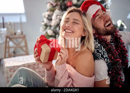 Glückliches junges Paar, das sich zurücklehnen, lachen und Geschenke vor dem weihnachtsbaum halten Stockfoto