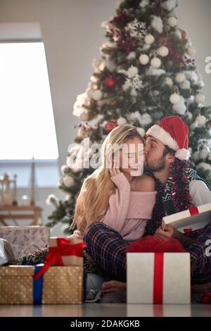 beardy Kerl küsst seine Freundin für weihnachtsgeschenk, zufrieden mit einem Geschenk, sitzt auf dem Boden Stockfoto