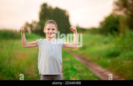 Kind nettes Mädchen zeigen Bizeps Geste der Kraft und Stärke im Freien. Fühlen Sie sich so kraftvoll. Mädchen Regeln Konzept. Stark und leistungsstark. Stockfoto