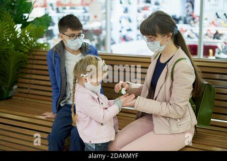 Mama behandelt die Hände von Kindern in einem Einkauf mit Desinfektionsgel Zentrieren Stockfoto