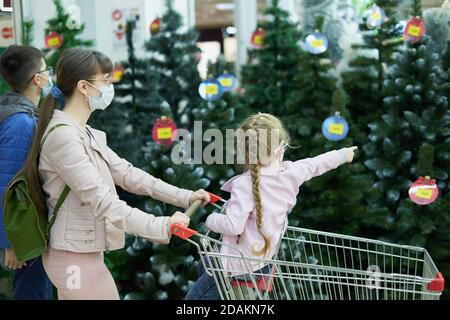 Mutter mit Kindern tragen Gesichtsmasken kaufen weihnachtsbaum in Das Einkaufszentrum Stockfoto