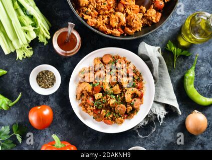 Kreolische Jambalaya mit Reis, geräucherten Würstchen, Hühnerfleisch und Gemüse auf dem Teller auf blauem Steingrund. Draufsicht, flach liegend, Nahaufnahme Stockfoto